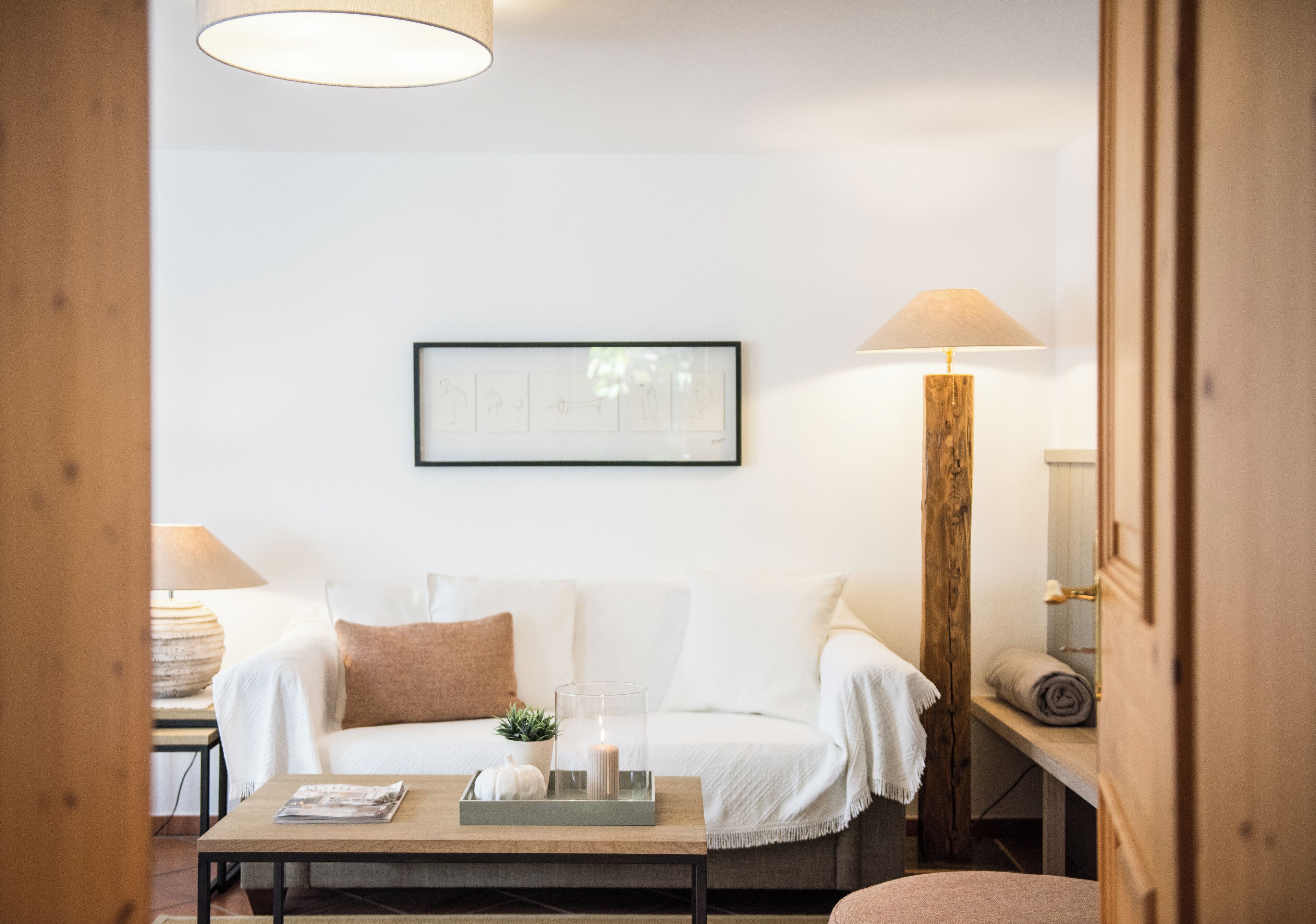 Une pièce chaleureuse avec un canapé blanc, une table basse en bois, une lampe et un tableau encadré au mur.