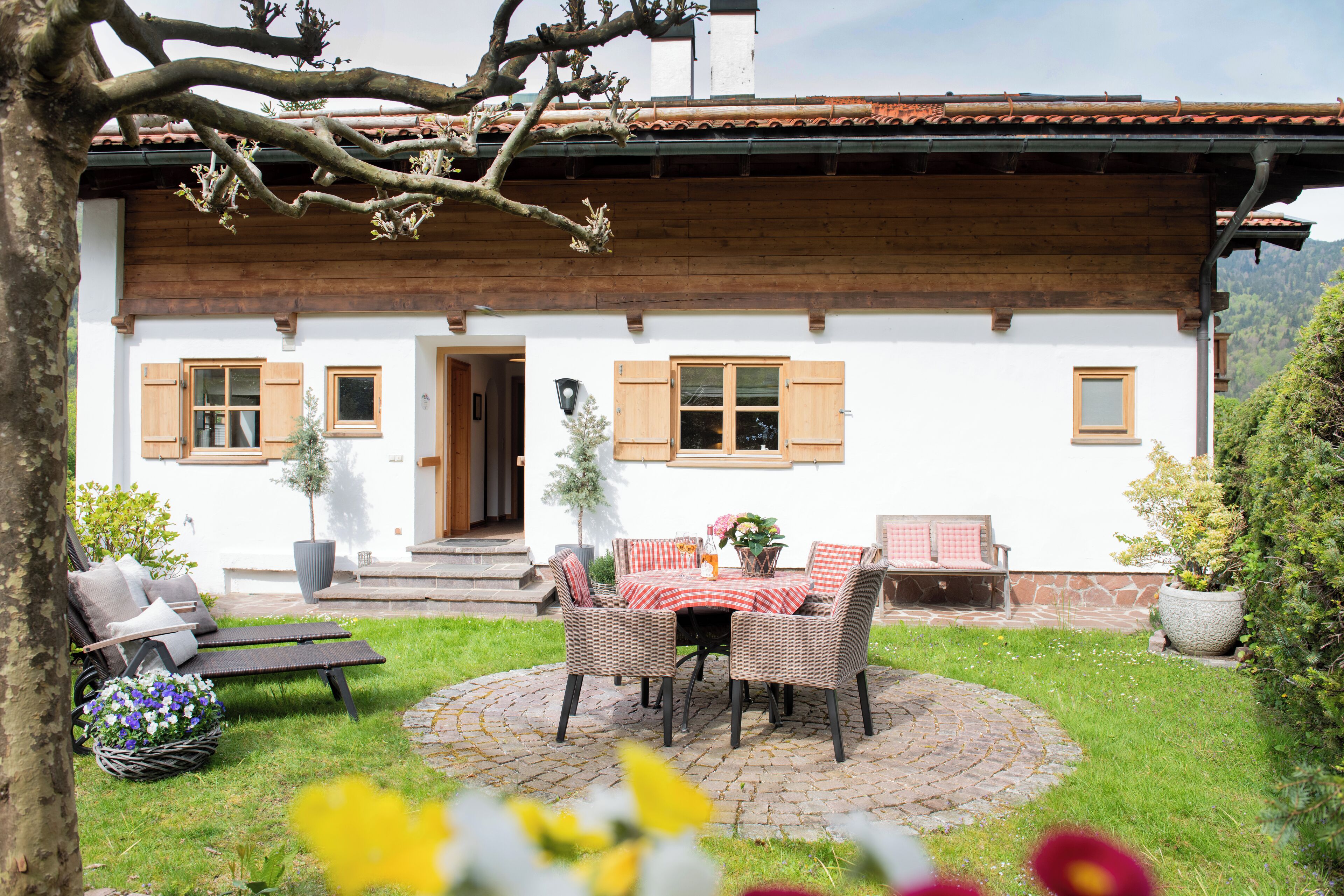 A white building with wooden shutters, a stone patio with wicker furniture, and a potted plant.
