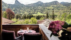 A wooden deck with a table set for two, overlooking a mountainous landscape with dense forests and a prominent peak. - Haus Lesch - Stilvolle Appartements mit tollem Bergblick in Kreuth am Tegernsee (Kreuth)