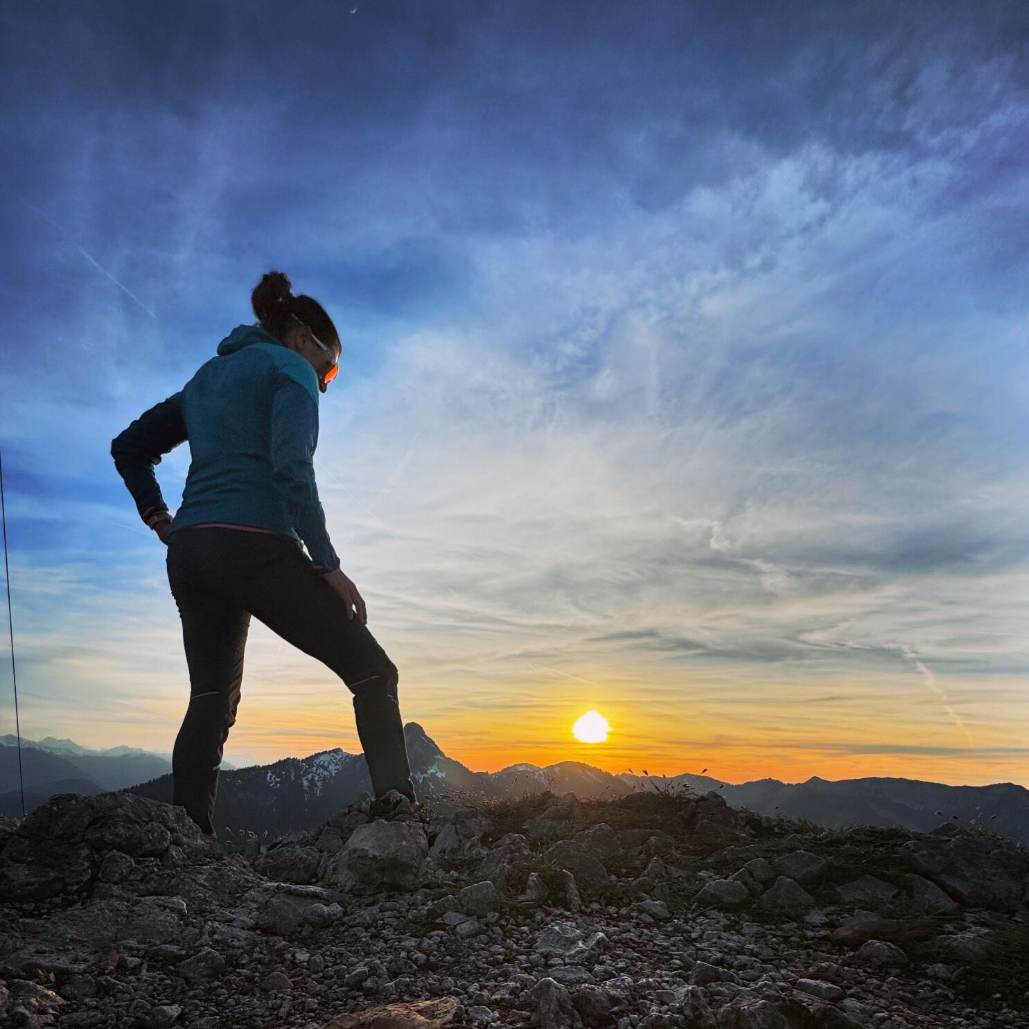 Une personne se tient debout sur un terrain rocheux, avec un coucher de soleil en arrière-plan.