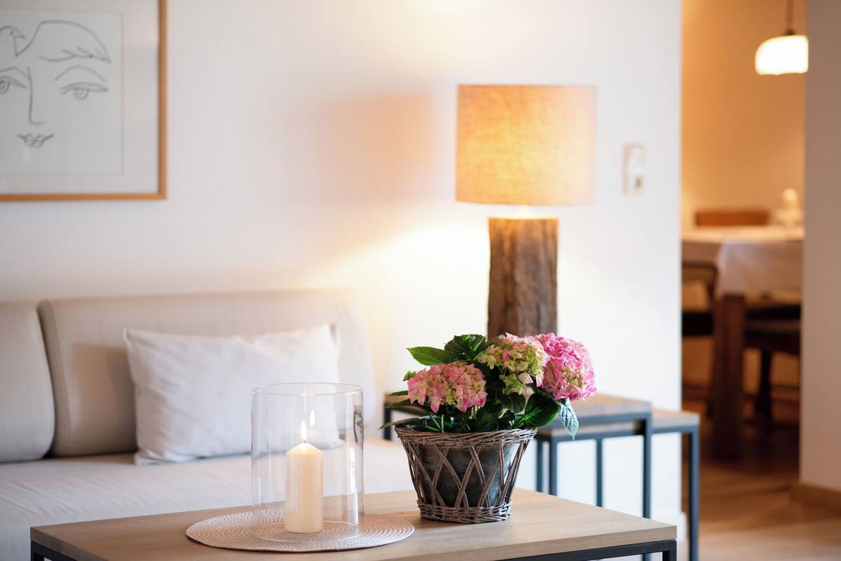 Ein gemütliches Zimmer mit einer Couch, einem Tisch mit Kerze und einem Blumenkorb.