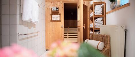 Un interior de madera con un perchero, un estante con toallas dobladas y una silla de mimbre.