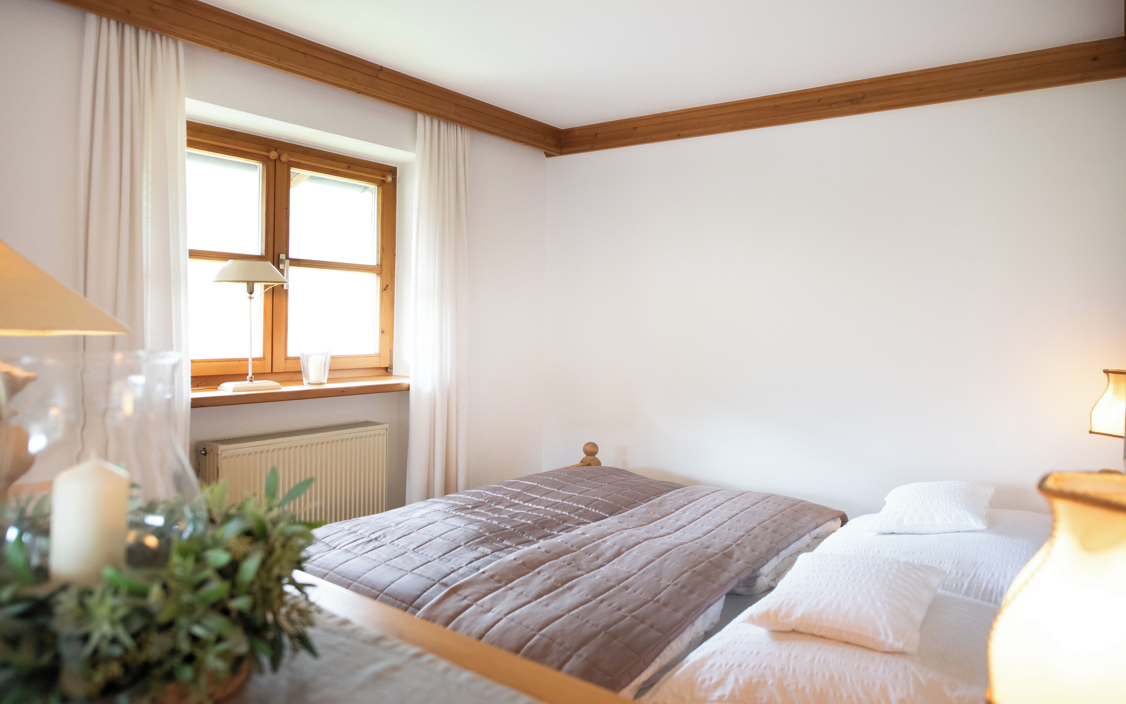 A bedroom with a bed, a window with curtains, a radiator, and a bedside table with a lamp.