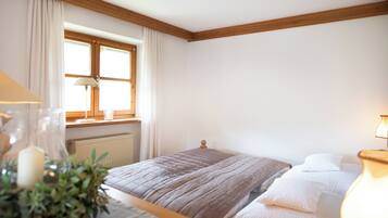 A bedroom with a bed, a window with curtains, a radiator, and a bedside table with a lamp.