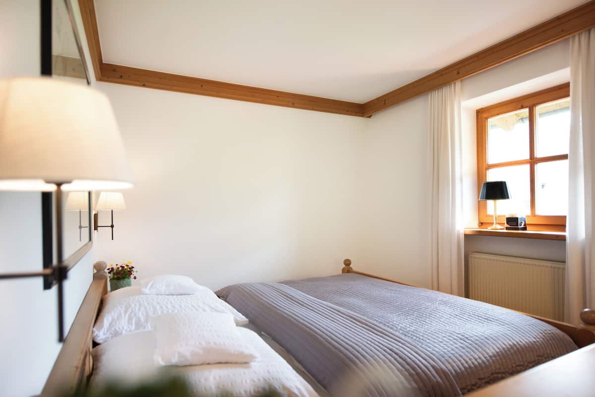 Ein Schlafzimmer mit einem Bett, einem Nachttisch, einer Lampe, einem Fenster mit Vorhängen und einer Heizung.