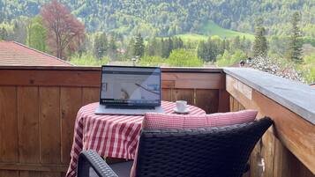 Una terraza de madera con una computadora portátil sobre una mesa, una silla de mimbre y un mantel a cuadros rojo y blanco.