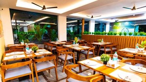 A restaurant with wooden tables and chairs, large windows with plants, and ceiling fans.