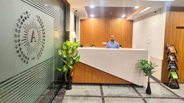 A reception desk with a wooden panel backdrop, a logo on the wall, and potted plants.
