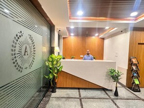 A reception desk with a wooden panel backdrop, a logo on the wall, and potted plants. - Hotel Aerotel  (Hyderabad)