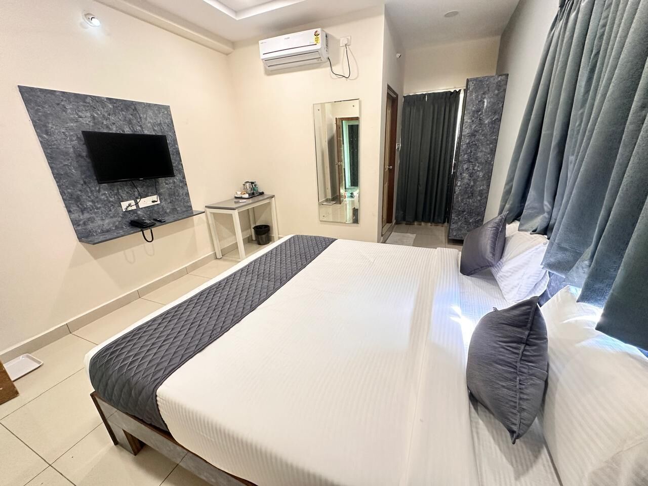 A hotel room with a large bed, a flat-screen TV mounted on a marble wall, a small bedside table, and a mirror.