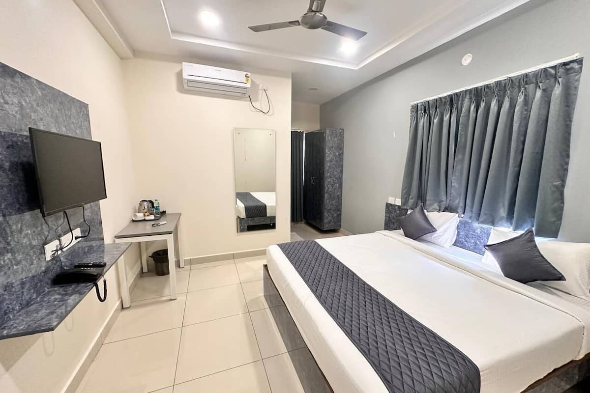 Ein modernes Hotelzimmer mit einem großen Bett, einem Flachbildfernseher, einem Schreibtisch mit Stuhl, einer Klimaanlage und einem Deckenventilator.