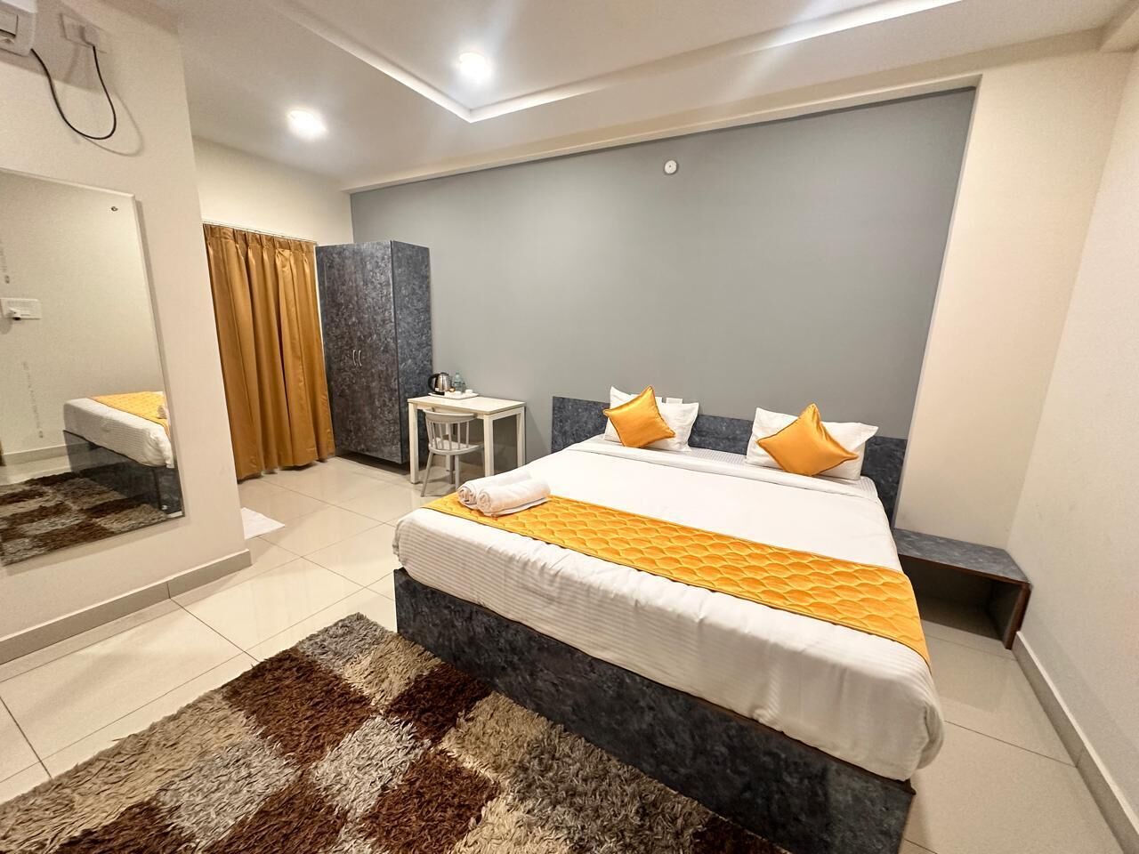 A modern hotel room with a large bed, a small desk, and a bathroom with a mirror and curtains.