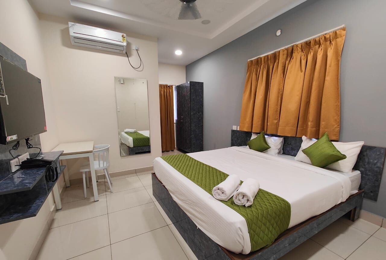 A hotel room with a bed, a desk, a chair, an air conditioning unit, and a mirror.