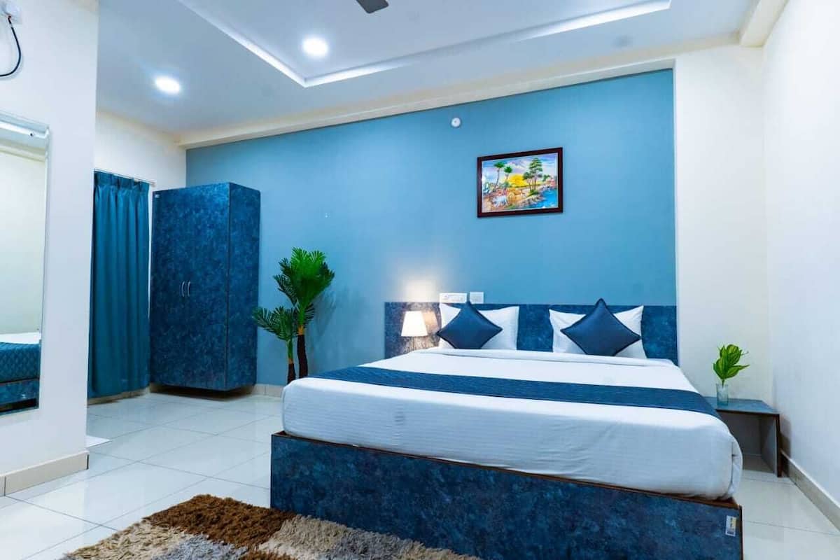 Ein Schlafzimmer mit einem Bett, einem Nachttisch, einer Wandlampe, einer blauen Wand, einem Gemälde und einem blauen Schrank.