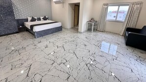 A spacious bedroom with a large bed, marble flooring, ceiling fans, and a window with curtains.