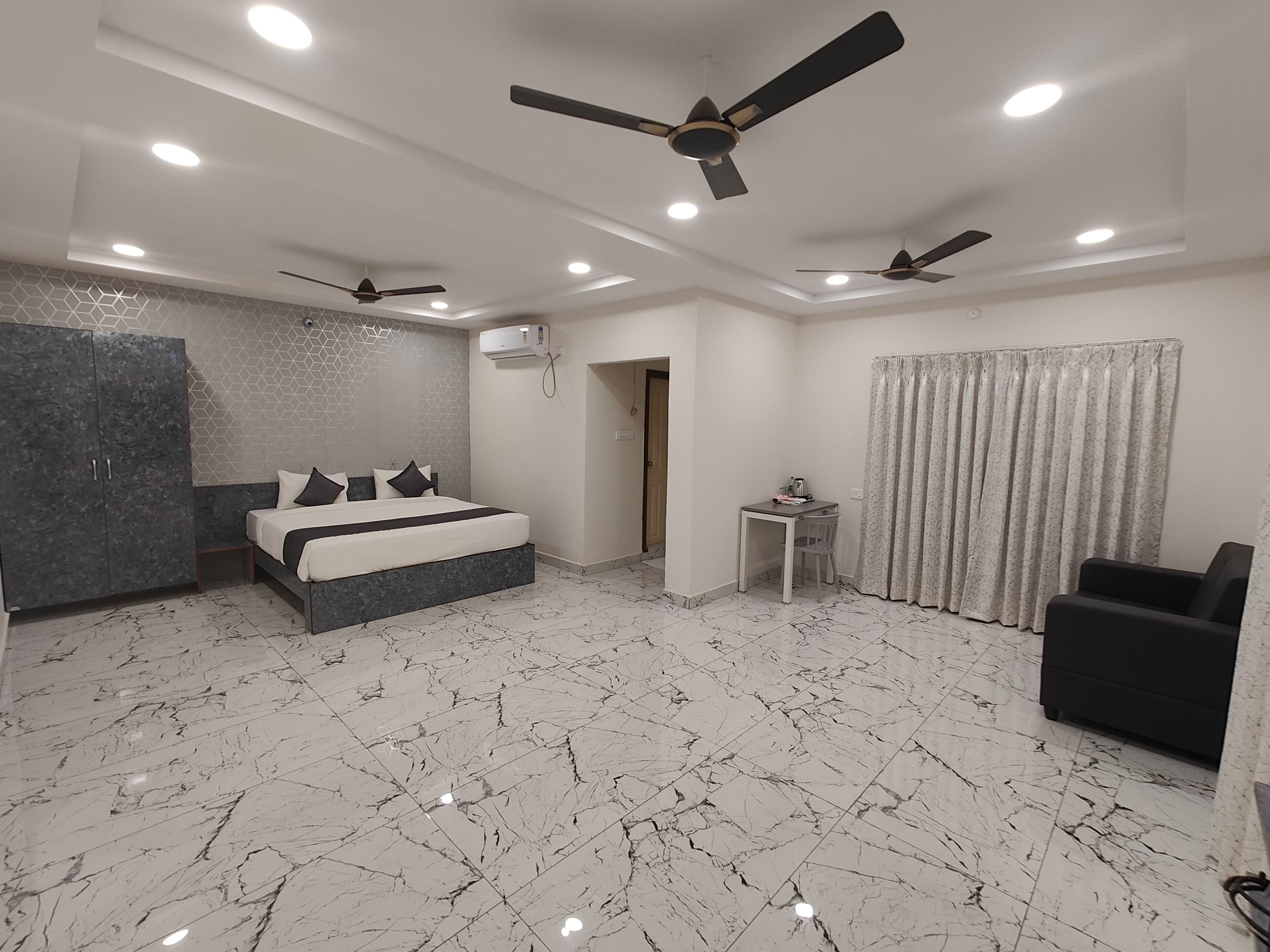 Une chambre moderne avec un grand lit, deux ventilateurs de plafond, une petite table et une chaise.