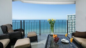 A balcony with wicker furniture, a vase with yellow flowers, a fruit bowl, and a glass of orange juice. - Grand Venetian Beachfront Condo (Puerto Vallarta)