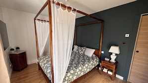 A four-poster canopy bed with a floral bedspread, a bedside table with a lamp, and a small nightstand with books. - Belle Villa Familiale Tout Confort à 15 mn des Plages (Cournonterral)