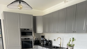 A modern kitchen with grey cabinets, a black countertop, a built-in oven, a coffee maker, and a sink. - Belle Villa Familiale Tout Confort à 15 mn des Plages (Cournonterral)