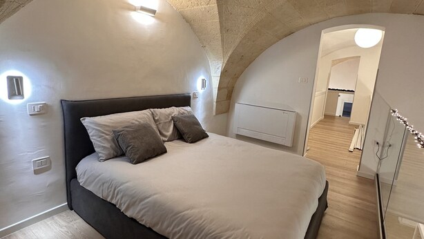 A bedroom with a large bed, a stone ceiling, and a wooden floor.
