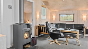 Ett mysigt vardagsrum med en vedeldad kamin, en lädersoffa, ett träbord och ett stort fönster med utsikt över träd.