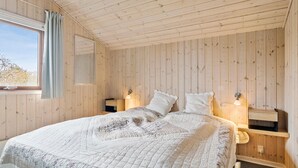 Ett sovrum med träpanel på väggarna, en säng, sänglampor och ett fönster med gardiner.