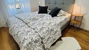 A bedroom with a bed, a bedside lamp, a white rug, and a window with curtains. - Allora (Split)