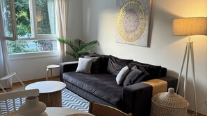 A modern living room with a black leather sofa, a round wooden coffee table, and a white dining table with woven placemats. - Allora (Split)