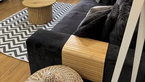A modern living room with a black sofa, a wooden coffee table, a woven ottoman, a white chair, and a bookshelf. - Allora (Split)
