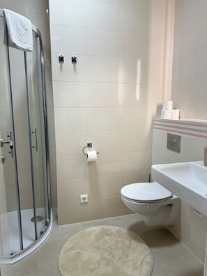 A bathroom with a glass-enclosed shower, a toilet, a sink, and a towel hanging on the shower door. - Allora (Split)