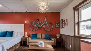 A modern bedroom with a bed, a sofa, a wooden coffee table, and a bicycle mounted on the wall. - Extended Stay | With Kitchen | Prescott Studio (PRESCOTT)