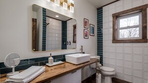 A bathroom with a wooden vanity, a white sink, a mirror, a toilet, and a window. - Extended Stay | With Kitchen | Prescott Studio (PRESCOTT)