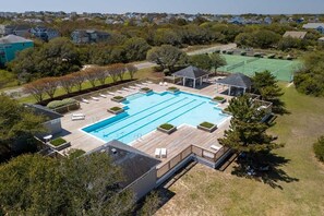 A swimming pool with a wooden deck, lounge chairs, and a tennis court in the background.