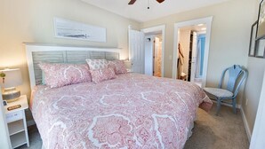 Un dormitorio con una cama grande, un ventilador de techo, una mesita de noche con lámpara y una silla.