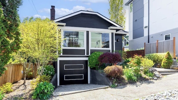 Une maison moderne à deux étages avec un garage, entourée d’un jardin bien entretenu et d’une clôture en bois.