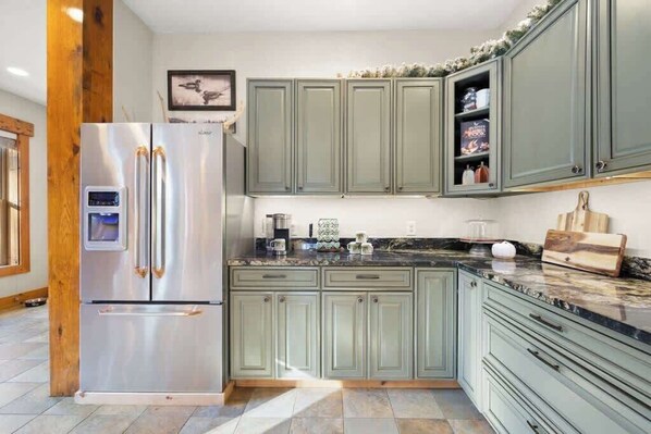 Una cocina con un refrigerador de acero inoxidable, armarios verdes, encimera de mármol y estructura de vigas de madera.