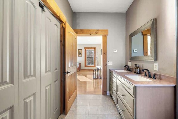 A hallway leading to a bathroom with two sinks and a large mirror. - The Lodge at Branch Pond (Ellsworth)