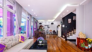 A modern living room with a sofa, coffee table, and decorative items. There is a staircase leading to another level, and a dining area with chairs and a table.