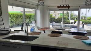Eine moderne Küche mit einer großen Kochinsel, einer Spüle und Blick auf die Terrasse.