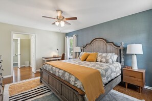 A bedroom with a bed, nightstands, a ceiling fan, and a view of the outside. - Hanahan Haven GameRoom Bikes FirePit Dog & Family Friendly (Hanahan)