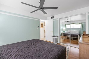 Een slaapkamer met een bed, een plafondventilator, een spiegel en een schuifdeur naar een andere kamer.