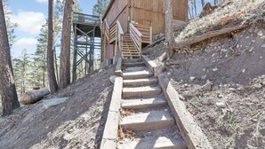 Une cabane en bois avec un escalier menant à une terrasse, le tout entouré d’arbres.