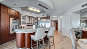 A modern kitchen with a central island, stainless steel appliances, and a curved ceiling. - Bella Luna 708 - Luxe 7th floor | Walk to Flora-Bama | Marina | 2 Bed 2 Bath (Orange Beach)