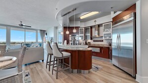 A modern kitchen with a central island, stainless steel appliances, and a view to the outside. - Bella Luna 708 - Luxe 7th floor | Walk to Flora-Bama | Marina | 2 Bed 2 Bath (Orange Beach)