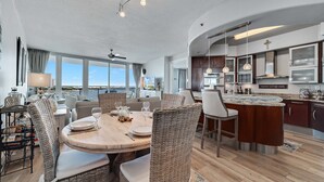 A modern kitchen with a large island, dining area with wicker chairs, and a view of the ocean. - Bella Luna 708 - Luxe 7th floor | Walk to Flora-Bama | Marina | 2 Bed 2 Bath (Orange Beach)