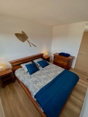 A bedroom with a wooden bed, two bedside tables, a wall-mounted lamp, and a wardrobe.