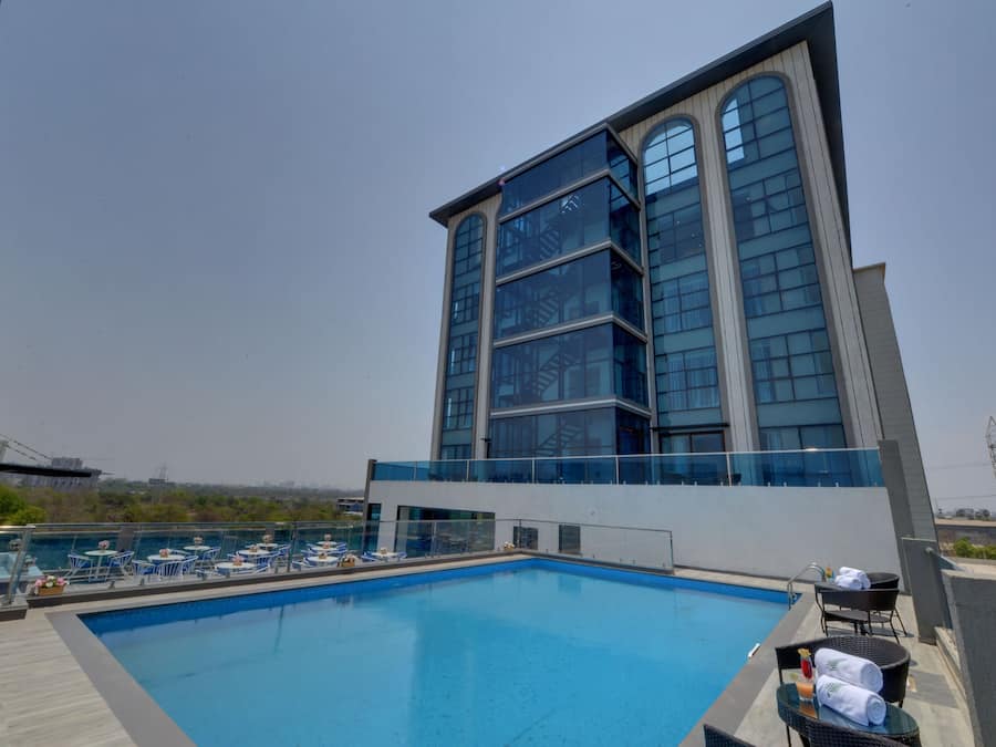 A rooftop pool area with lounge chairs and a glass balustrade overlooking a cityscape.