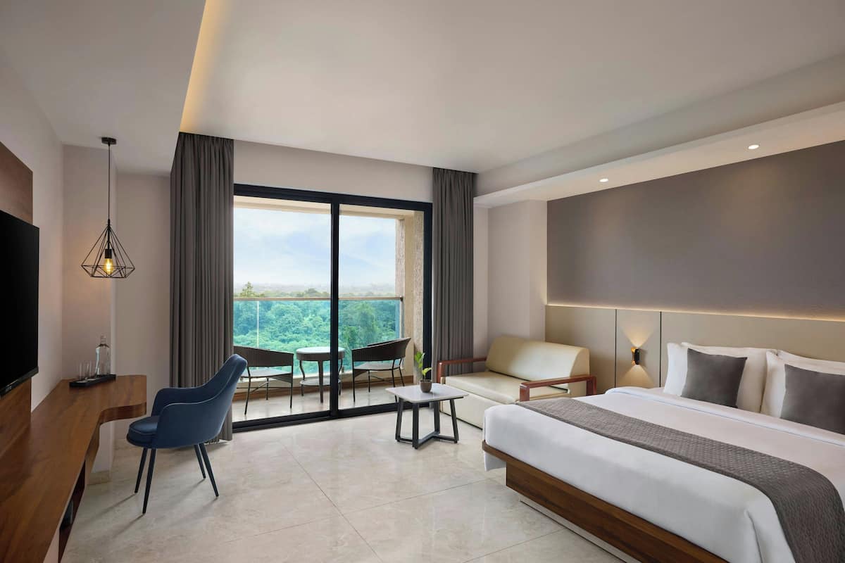 A modern hotel room with a large bed, a desk with a chair, a small table, a sofa, and a TV.