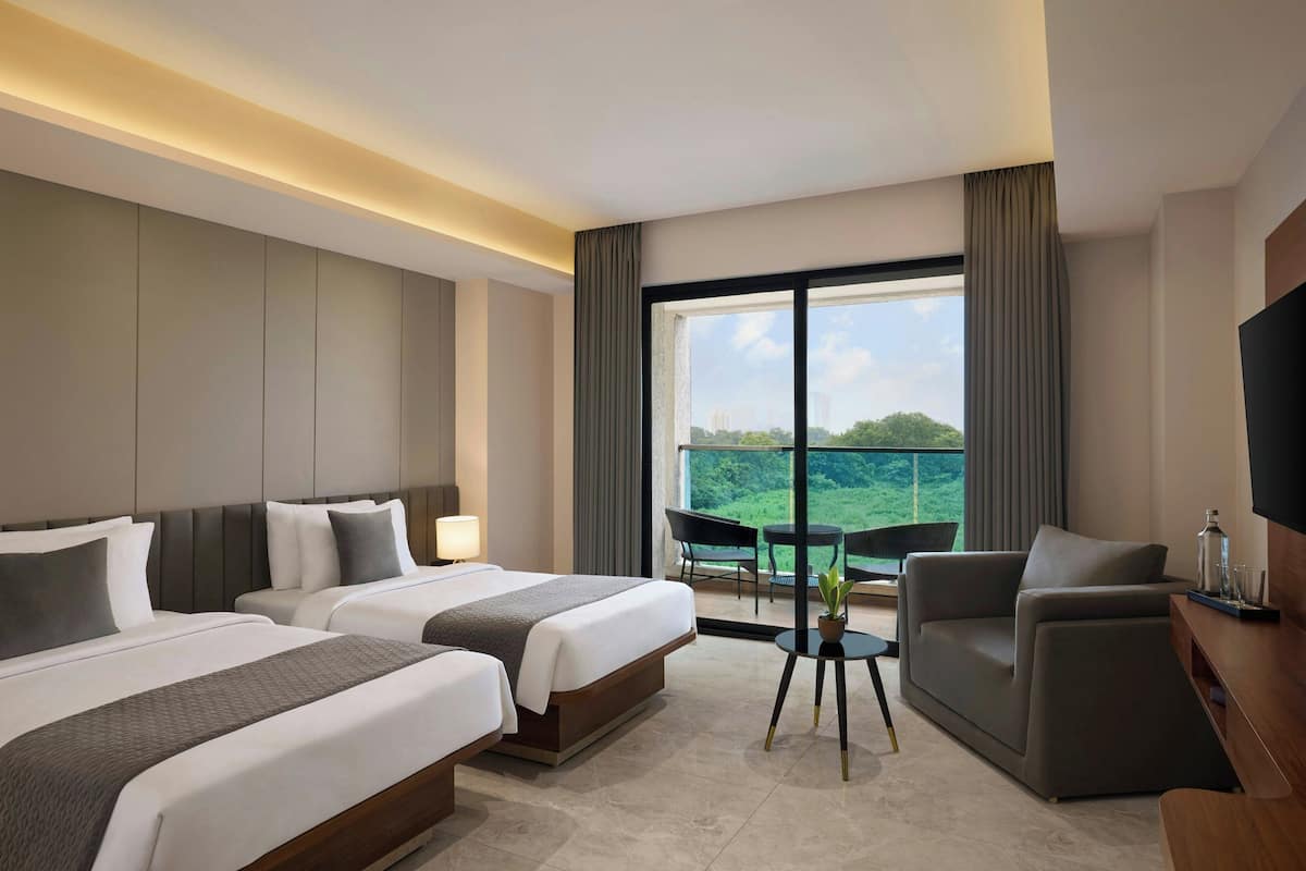 A hotel room with two beds, a sofa, a TV, a balcony with a view, and a dining table.