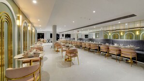 Een ruim restaurant met lange tafels en stoelen, een modern interieur en een grote spiegelwand.
